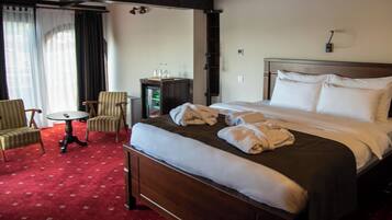 A hotel room with a large bed, two chairs, a small table, and a minibar.