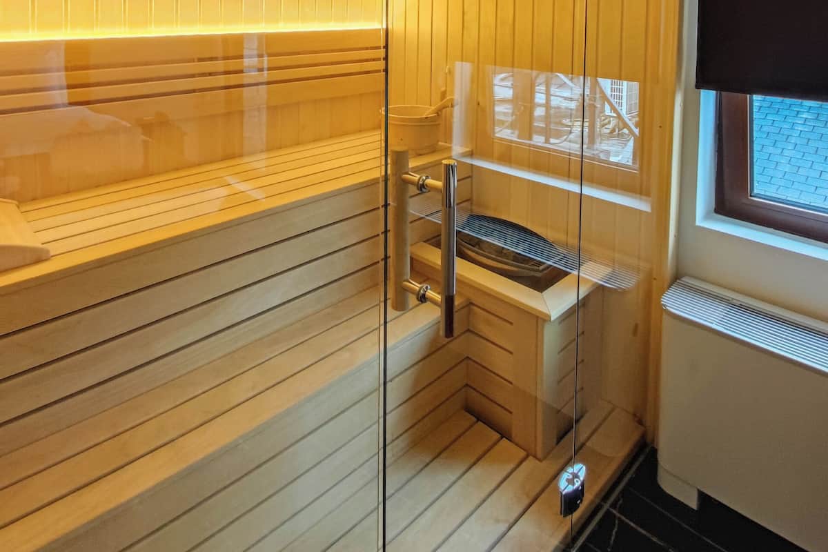 Una sauna con paredes de madera y una partición de vidrio, un banco y una lámpara colgante.