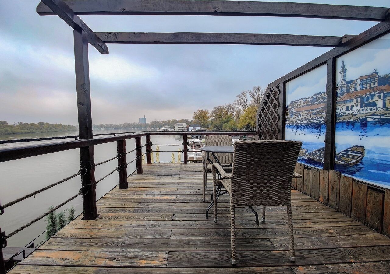 Un pontile in legno con tavolo e sedie, affacciato su uno specchio d'acqua con uno skyline sullo sfondo.
