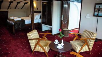 Una habitación de hotel con una cama, dos sillones, una mesita con un jarrón de flores y una alfombra roja.