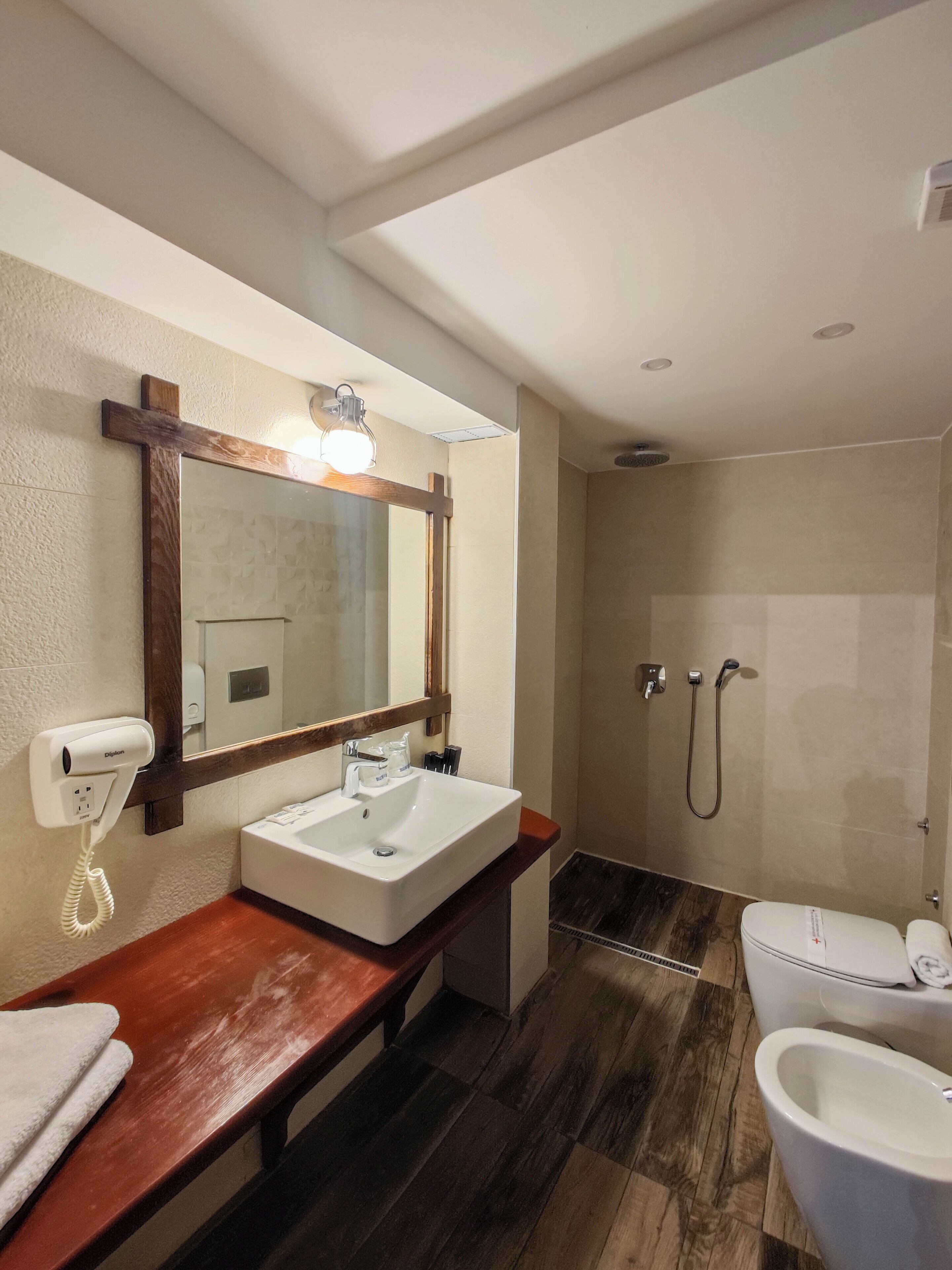 Ein Badezimmer mit einem Holzkosmetikschrank, einem großen Spiegel, einem Waschbecken, einer Toilette und einem Duschbereich.