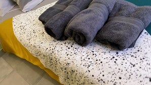A bed with a white and black speckled blanket, a yellow skirt, and three folded dark towels. - Charming bright apartment with large living room and 2 bedrooms - Comfort guaranteed (Trévillach)