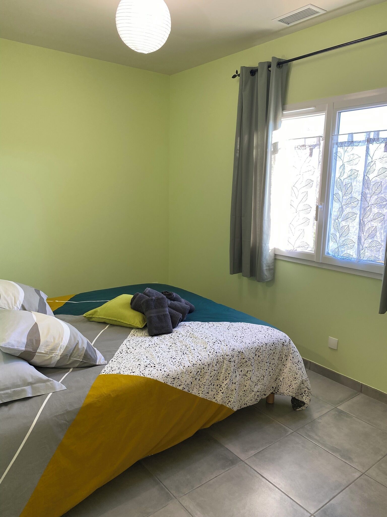 Un dormitorio con cama, almohadas, una ventana con cortinas y una lámpara en el techo.