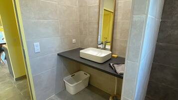 Un baño con un lavamanos blanco, un espejo y una zona de ducha.
