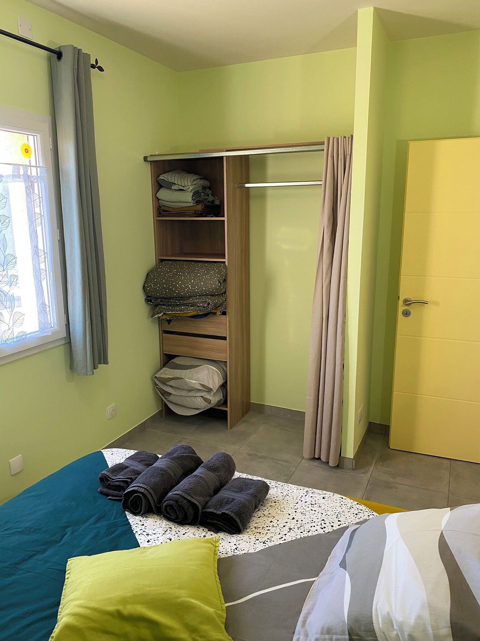 Un dormitorio con cama, armario, ventana con cortinas y puerta.