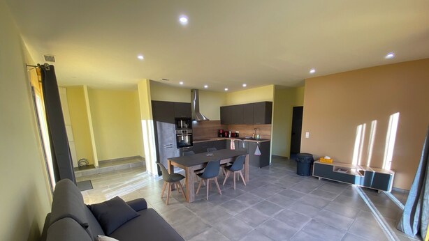A modern living room with a dark-colored sofa and a dining area with a table and chairs. - Charming bright apartment with large living room and 2 bedrooms - Comfort guaranteed (Trévillach)