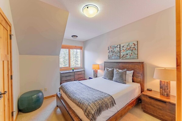 Une chambre à coucher avec un lit en bois, une table de chevet, une lampe, une fenêtre et un tableau au mur.