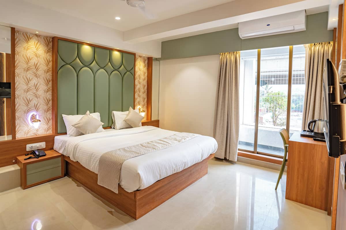 A modern hotel room with a large bed, a bedside table with a phone, a flat-screen TV, and a view of the outdoors through a large window.