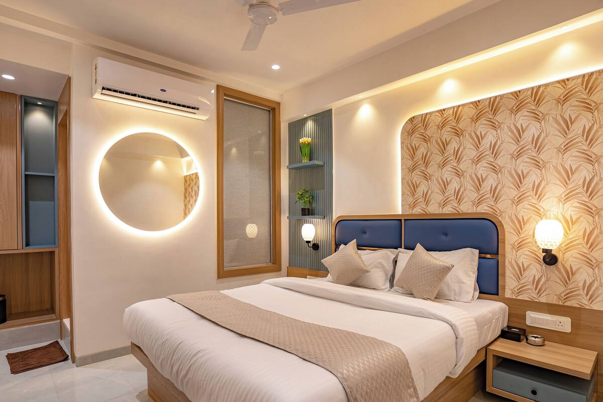 A modern bedroom with a large bed, bedside tables, a wall-mounted air conditioner, and a circular mirror.