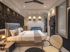A modern bedroom with a large bed, a blue sofa, a desk with a telephone, and a ceiling fan. - Hotel Supreme Inn (Thane)