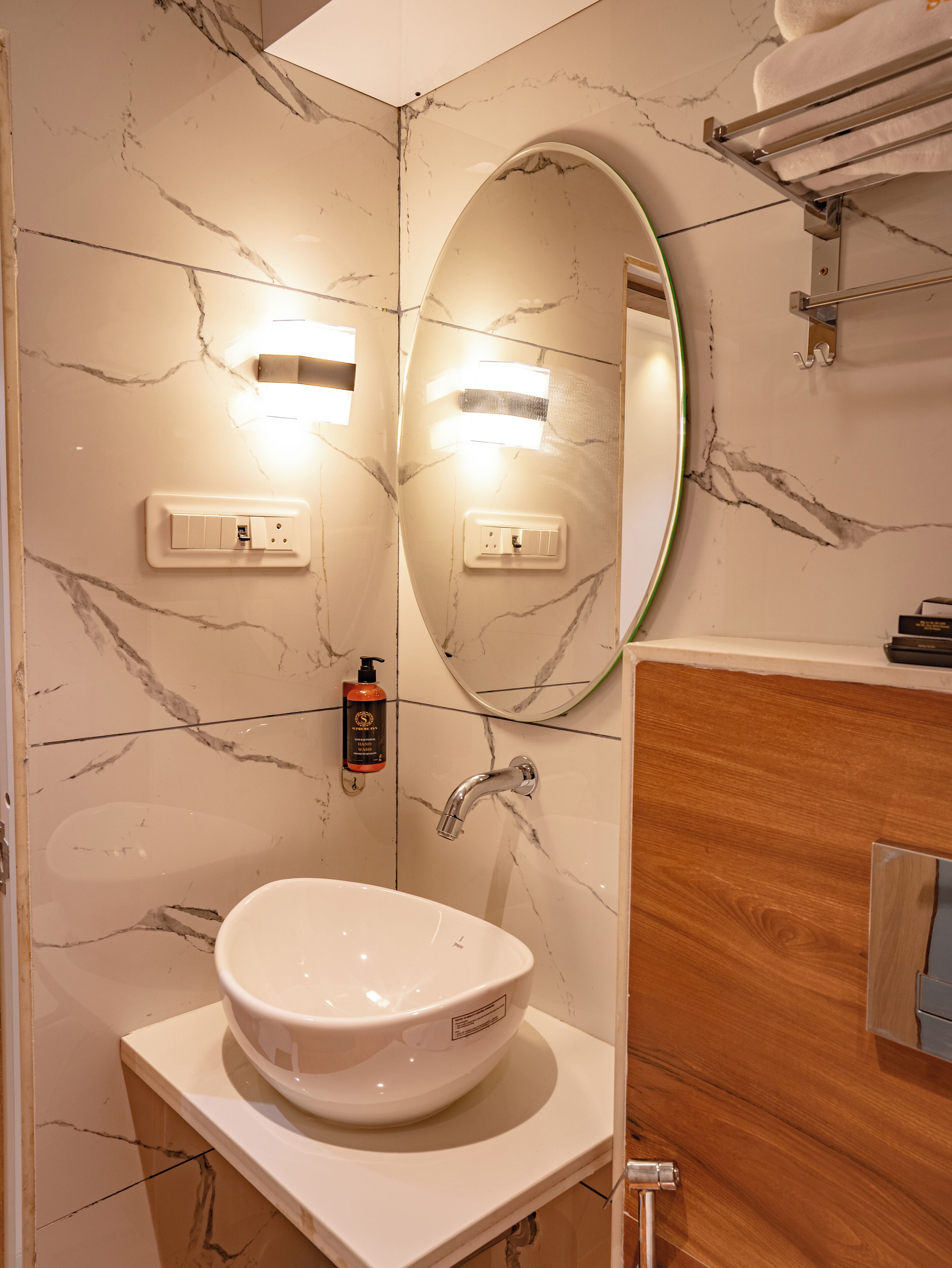 Un baño con pared de mármol, un espejo redondo, un lavamanos blanco y un mueble de tocador de madera.