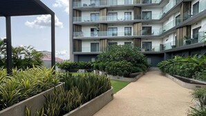 Un edificio residencial de varios pisos con balcones, una galería techada y zonas ajardinadas con plantas.