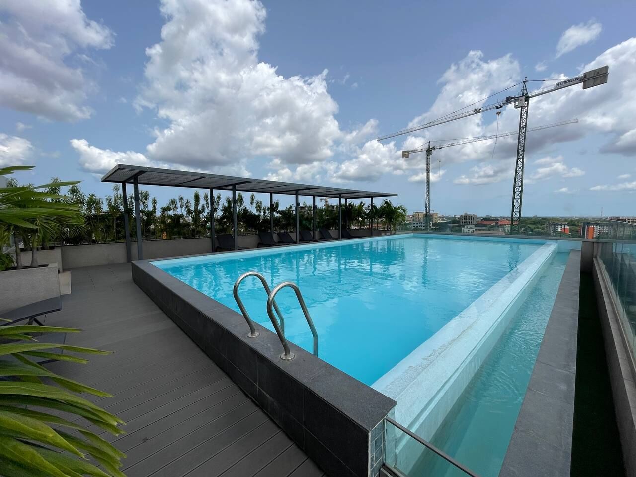 Piscina no terraço com área de estar coberta, rodeada por palmeiras e céu claro.