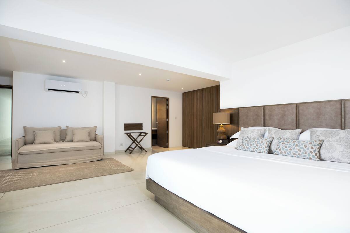 Quarto de hotel moderno com uma cama grande, um sofá e um aparelho de ar condicionado.