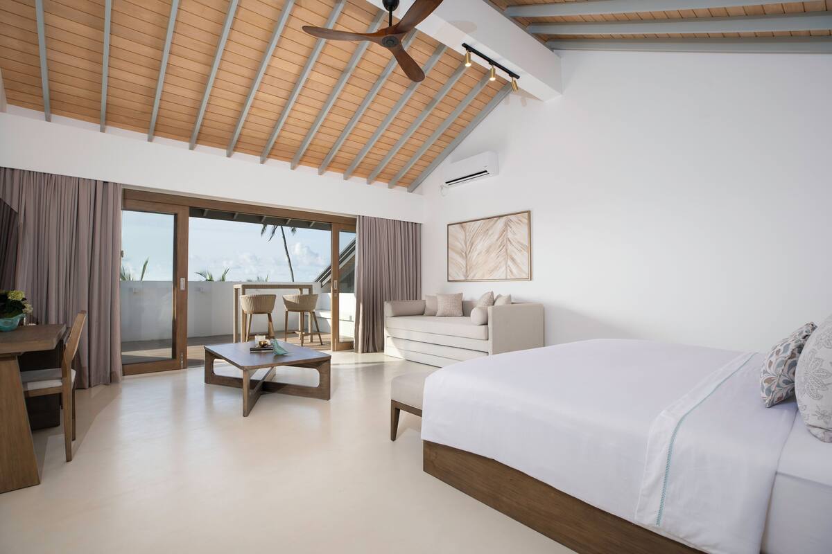 Quarto moderno com uma cama grande, um sofá, uma mesa de jantar e vista para uma varanda através de uma porta de correr.