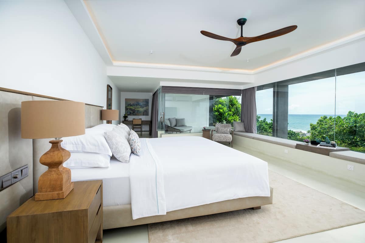 Quarto moderno com uma cama grande, ventilador de teto e vista para o oceano.
