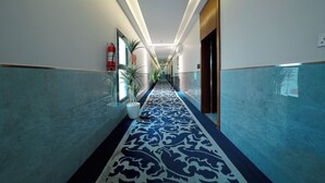 A hallway with a patterned carpet, potted plants, and a fire extinguisher. - Celine Home Serviced apartment -Tuwaiq  (Riyadh)