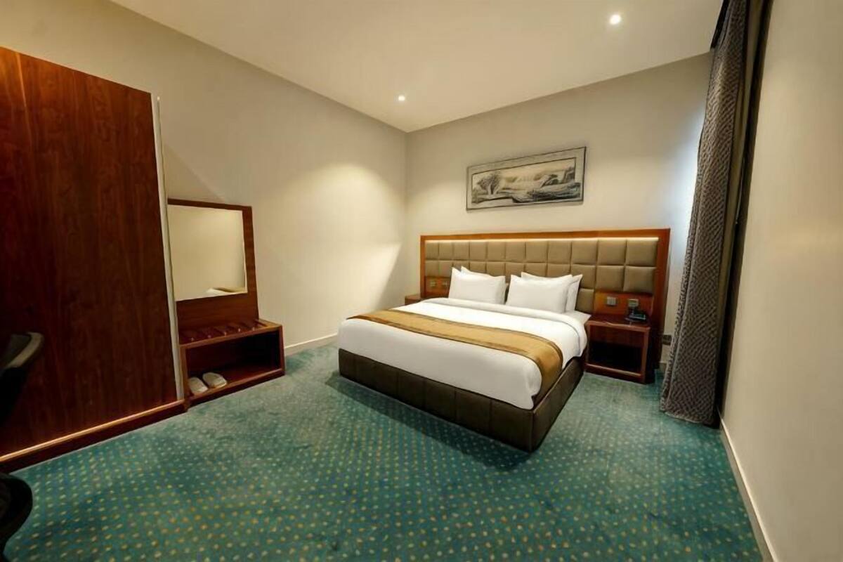 Een hotelkamer met een groot bed, een houten garderobe, een zithoekje en een schilderij aan de muur.