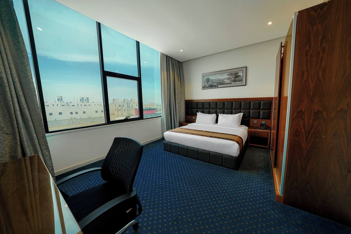 Een hotelkamer met een groot raam, een bed, een bureau en een stoel.