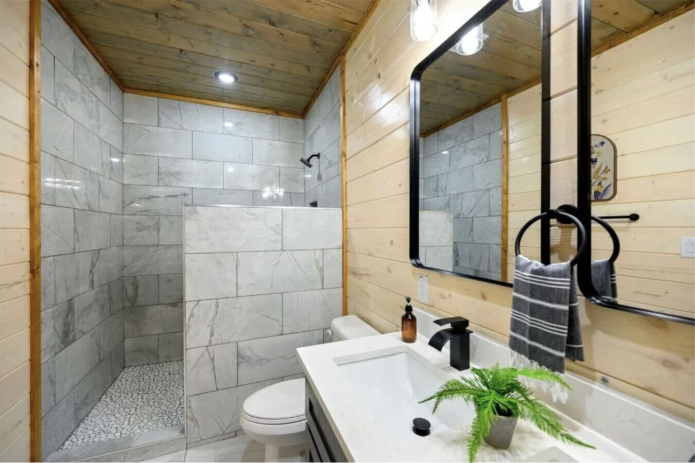 Ein Badezimmer mit Dusche, Toilette, Waschbecken und Spiegel.