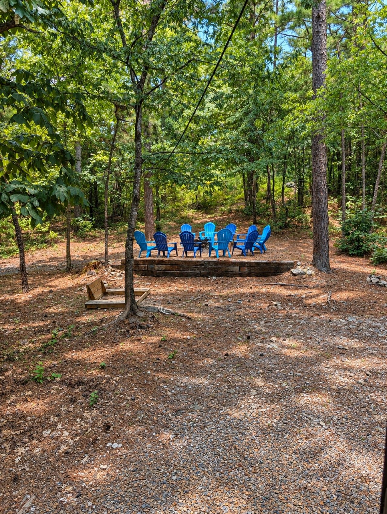 A forested area with a wooden deck and several blue chairs arranged for seating.
