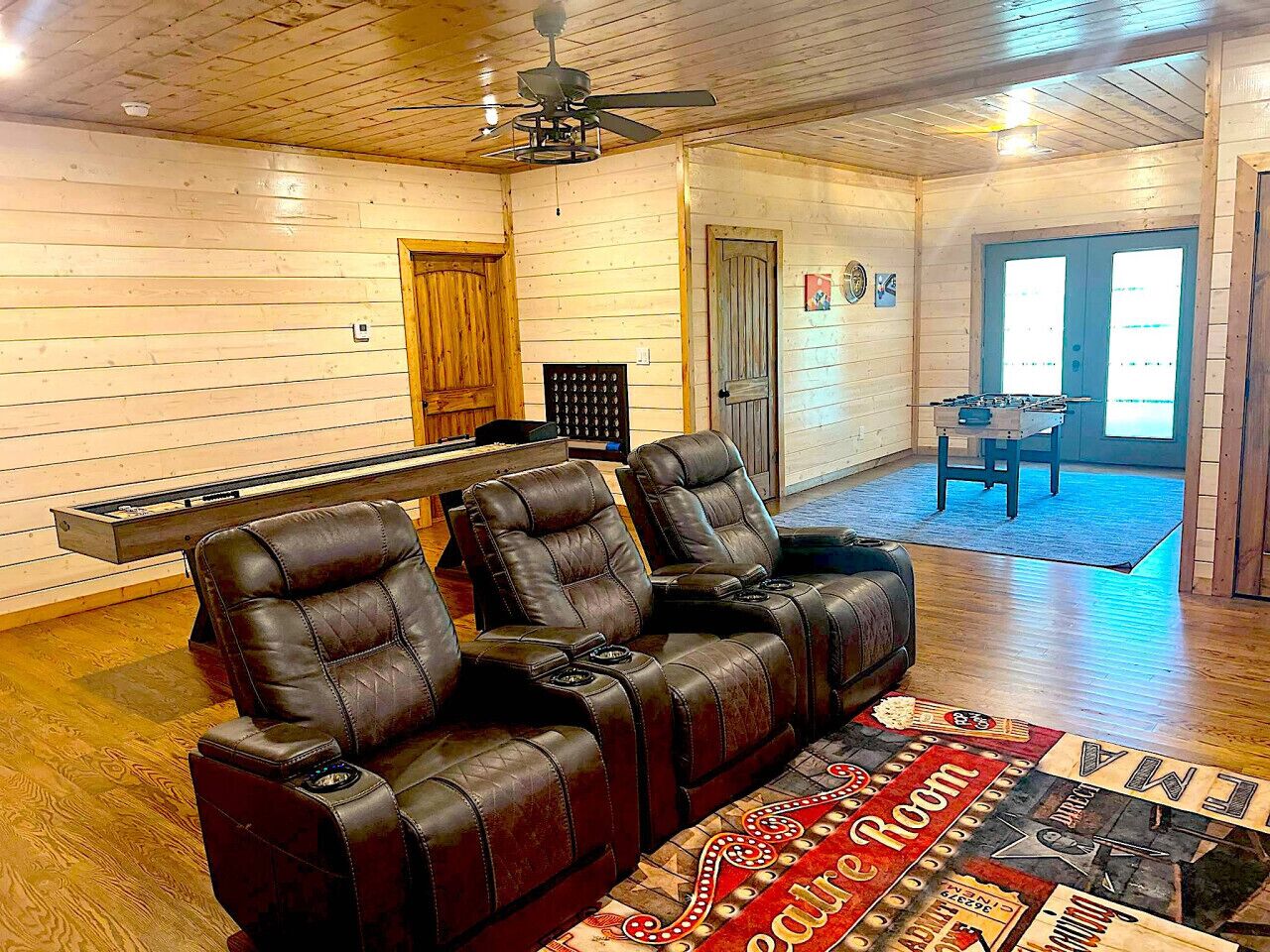 A room with wooden walls and a ceiling fan, featuring a sofa with leather chairs, a small table, and a rug.