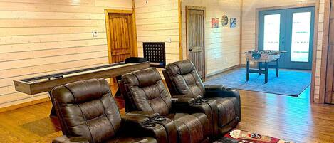 A room with wooden walls and a ceiling fan, featuring a sofa with leather chairs, a small table, and a rug.