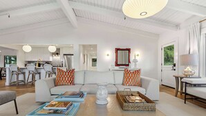 A spacious living room with a sofa, coffee table, and a dining area in the background. - LUX Private Modern Villa | Pool, Spa, & Dogs OK (Calistoga)