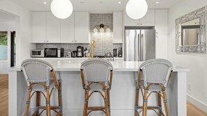 A modern kitchen with white cabinetry, a central island with bar stools, a stainless steel refrigerator, and pendant lighting. - LUX Private Modern Villa | Pool, Spa, & Dogs OK (Calistoga)