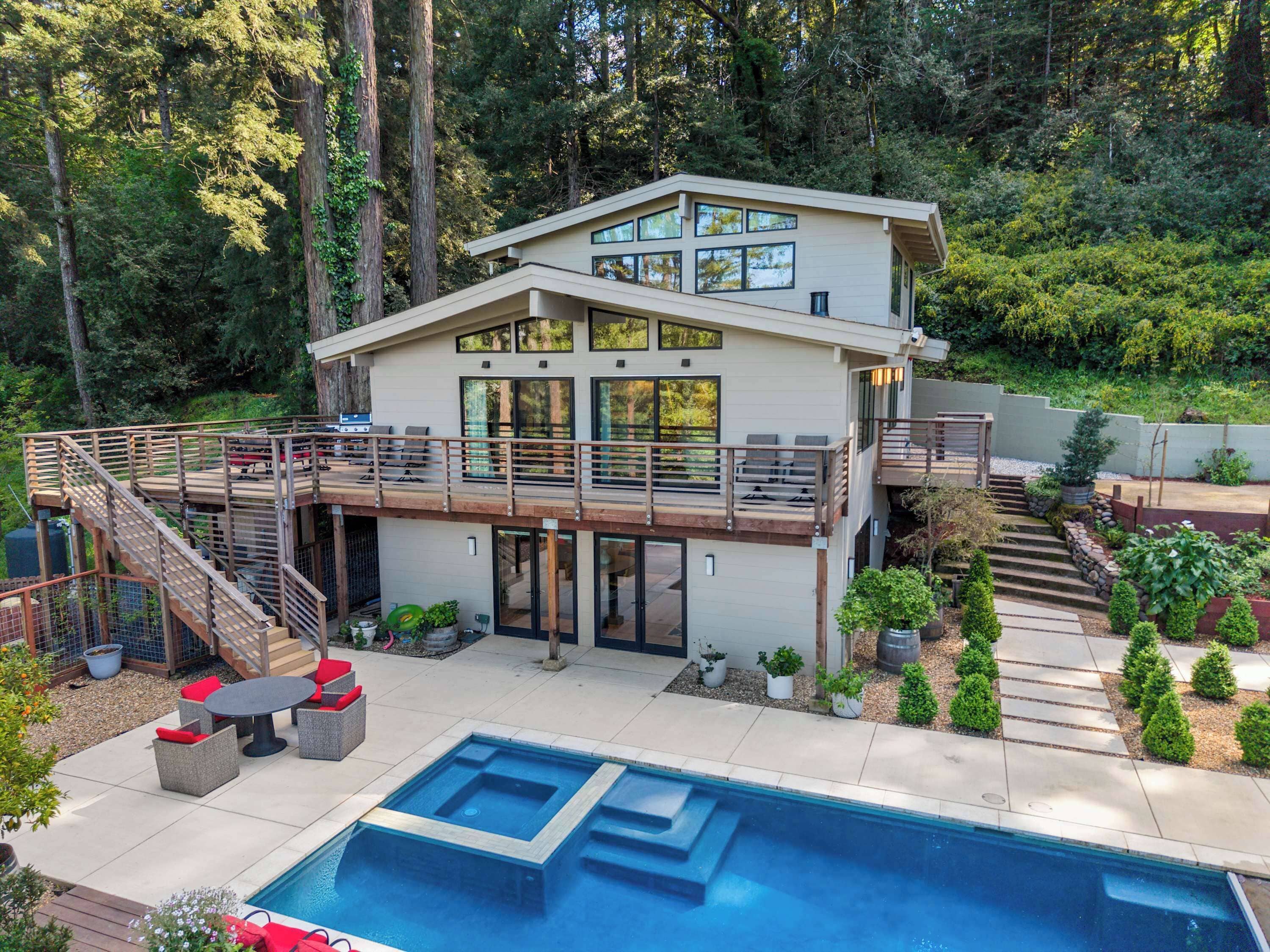 Une maison moderne à deux étages, dotée d’une terrasse, d’une piscine et bordée d’une forêt.