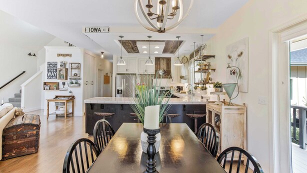 Una cocina moderna con una isla central, iluminación colgante y una zona de comedor con mesa y sillas.
