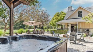 Un jacuzzi con cubierta de madera, mobiliario exterior y una casa al fondo.