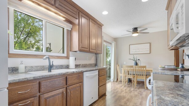 A kitchen with wooden cabinets, a built-in dishwasher, a granite countertop, and a ceiling fan. - The Modern Nest: Near Interstate, making it easy to get anywhere in Sioux Falls. (Sioux Falls)