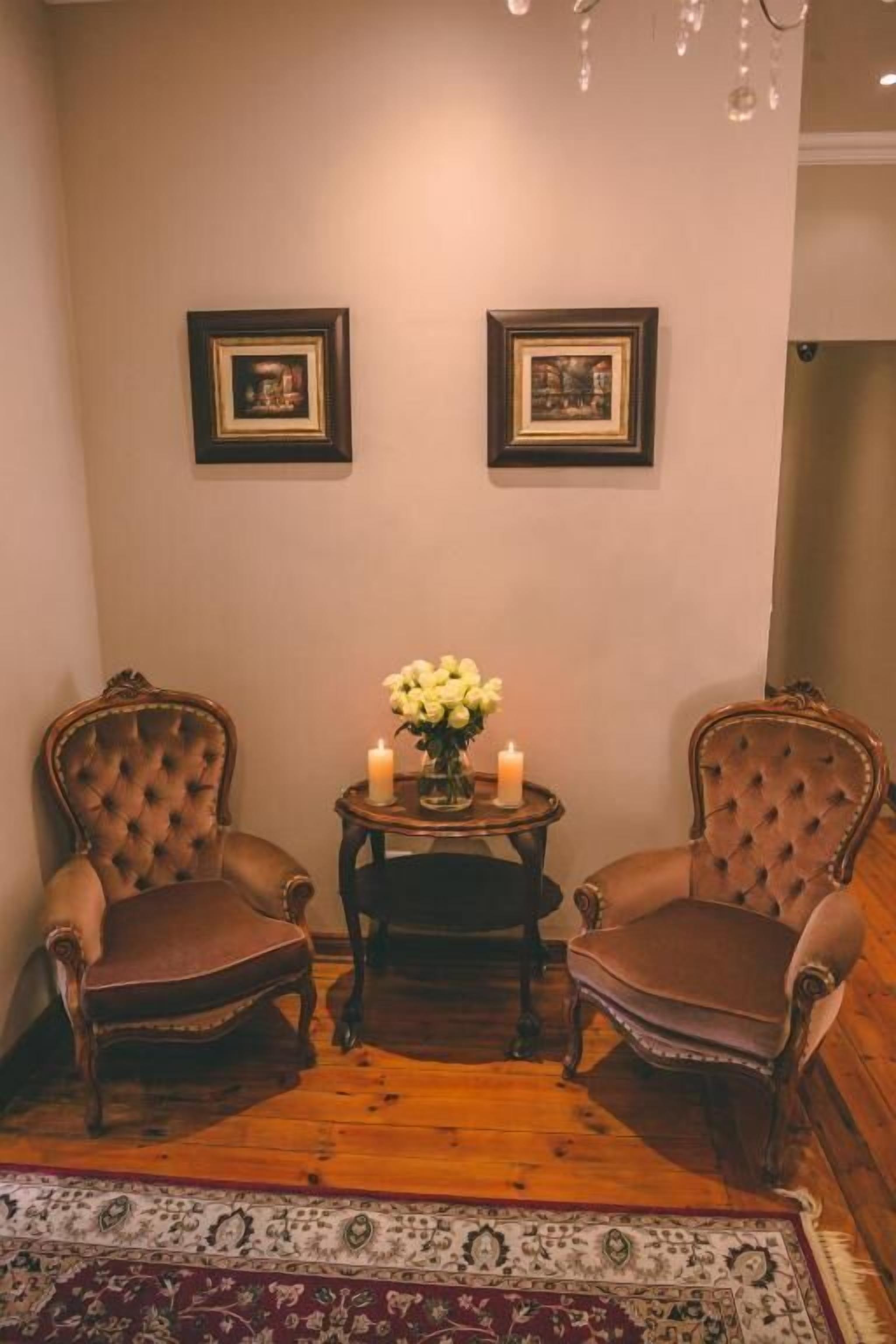 A room with two upholstered chairs, a small round table with candles, and a patterned rug.