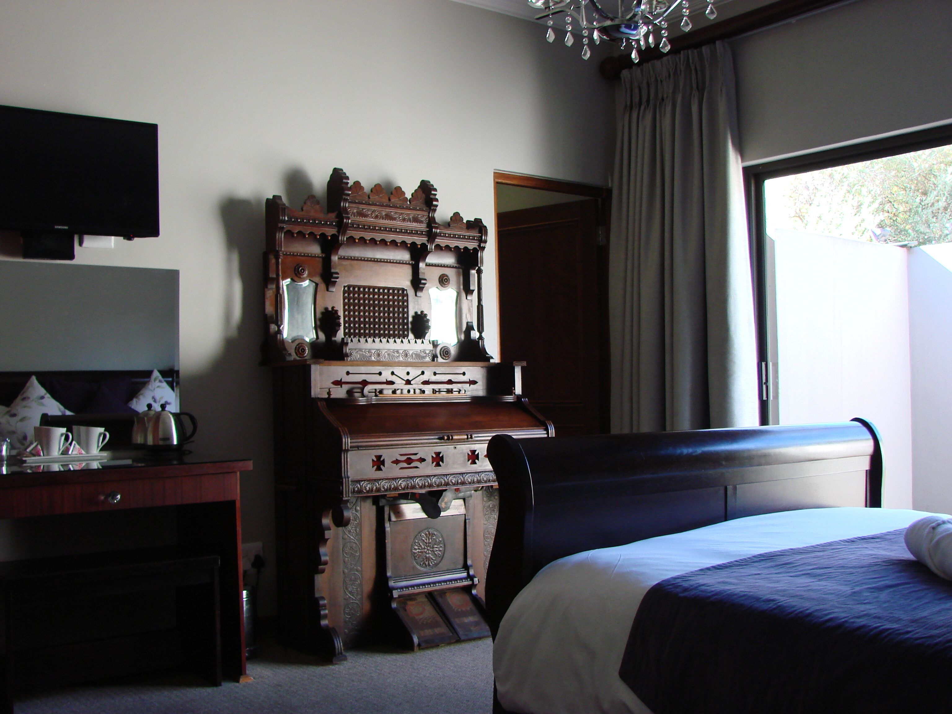 A hotel room with a bed, a desk with a flat-screen TV, a wooden cabinet, and a window with curtains.