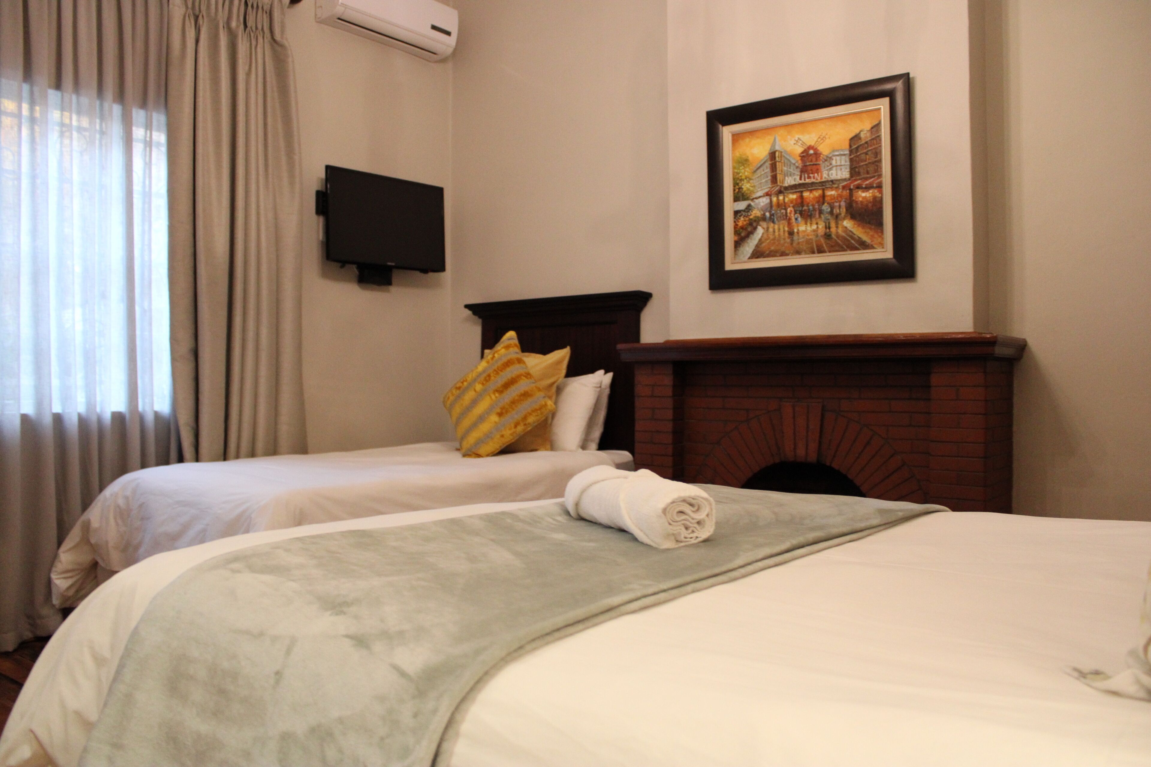 A hotel room with two beds, a fireplace, a painting, and a TV on the wall.
