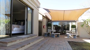 A hotel entrance with a covered patio area, a bed visible through the sliding glass door, and outdoor seating. - Abiénto Guesthouse (Bloemfontein)