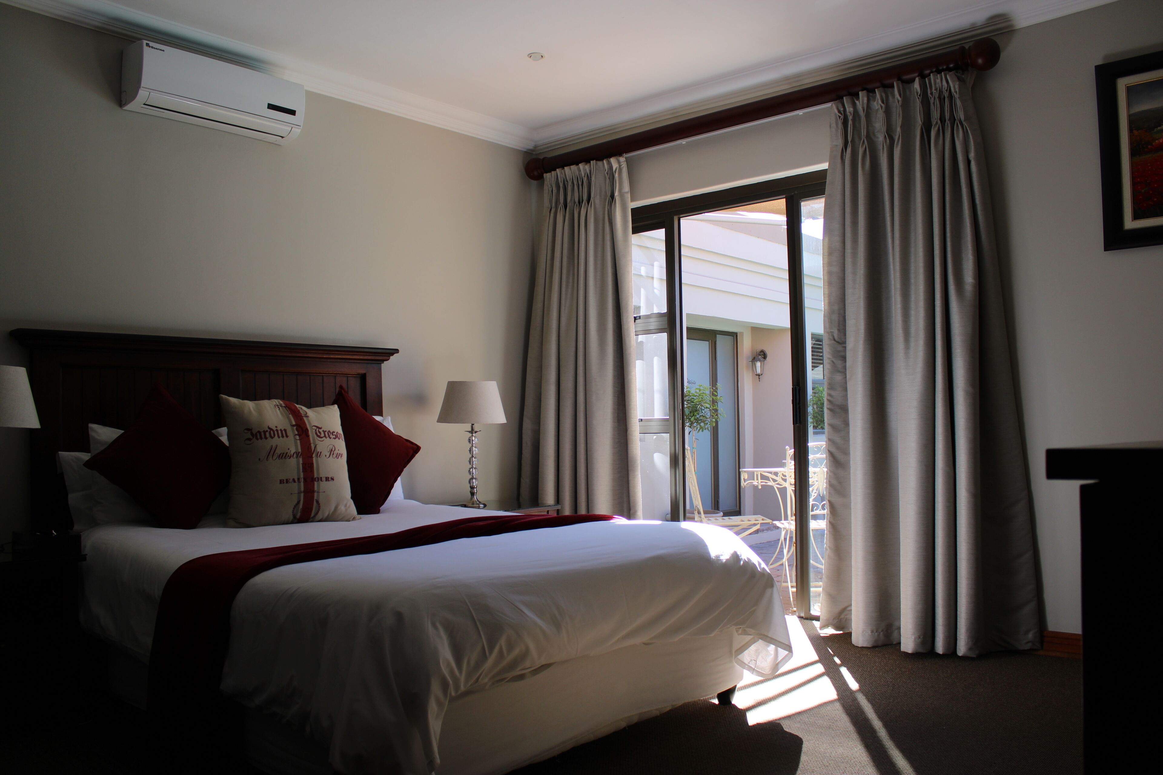 A hotel room with a large bed, a wooden headboard, a window with curtains, and an air conditioning unit on the wall.