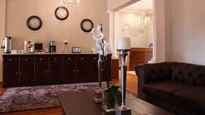 A living room with a dark brown sofa, a coffee table, and a decorative vase with white flowers. There are two clocks on the wall and a chandelier hanging from the ceiling. - Abiénto Guesthouse (Bloemfontein)