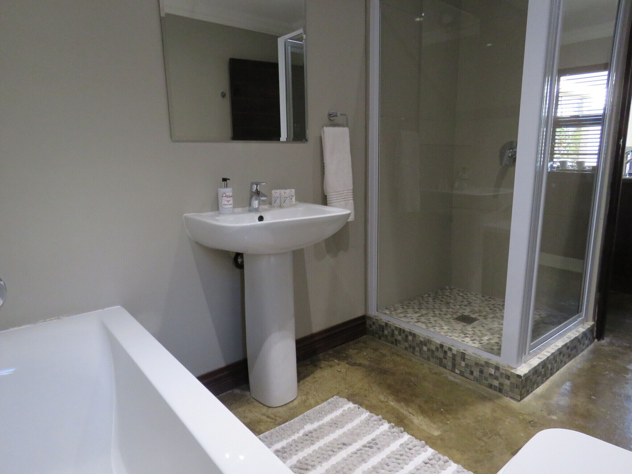 A bathroom with a white pedestal sink, a mirror above it, a glass-enclosed shower, and a white bathtub.