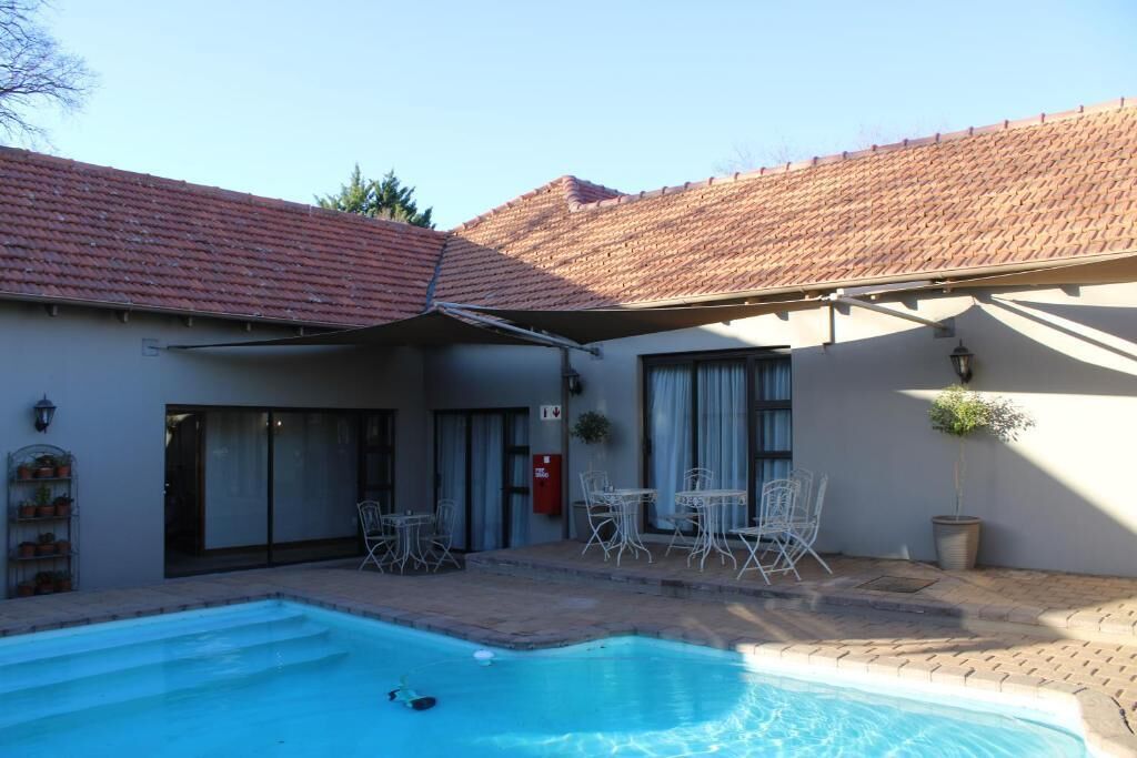 A swimming pool with a tiled roof, a covered patio area with outdoor seating, and a building with a tiled roof and a fire extinguisher on the wall.