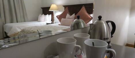 A hotel room with a bed, a nightstand, a lamp, a coffee maker, and a breakfast tray with cups and a glass.
