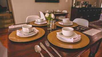 Una mesa de comedor dispuesta con tazas y platillos blancos, platos dorados, cubiertos y un jarrón con flores.