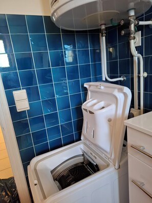 Eine kompakte, weiße Waschmaschine mit Frontlader in einem Badezimmer mit blauen Fliesen.