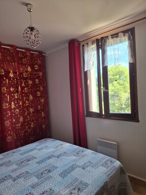 Ein Schlafzimmer mit einem Bett, einem Fenster mit Vorhängen und einer Pendelleuchte.
