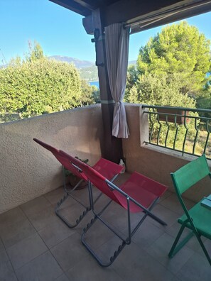 Een balkon met een rode klapstoel, een groene klapstoel en een potplant.