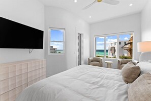 A modern bedroom with a large bed, a flat-screen TV, a view of the sea, and a balcony with seating.