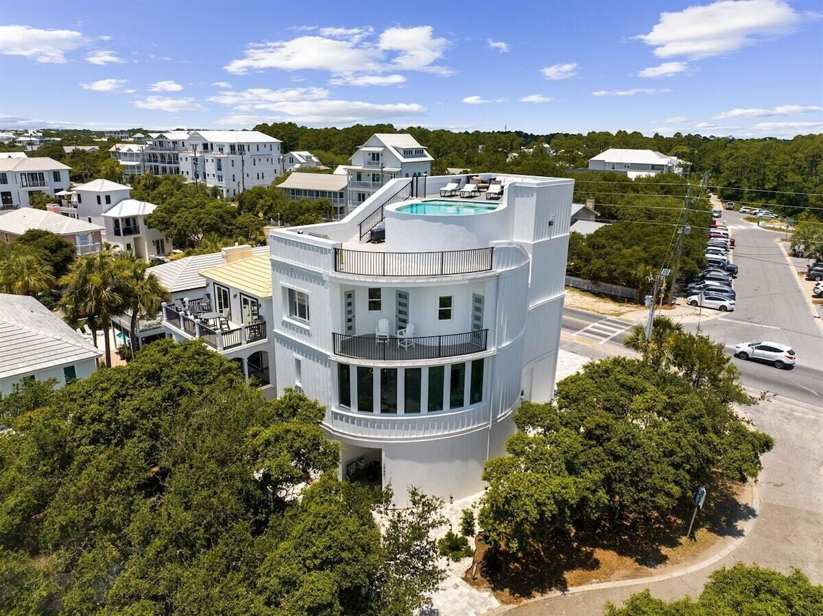A multi-story building with a pool on the upper level, surrounded by trees and other residential buildings.
