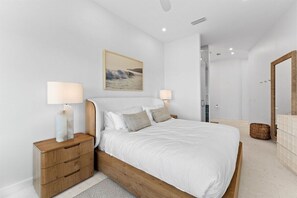 A modern bedroom with a large bed, bedside tables, a painting on the wall, and a bathroom visible through an open door. - 30A | Rooftop Pool | Gulf Views | 2 Min To Beach! (Santa Rosa Beach)