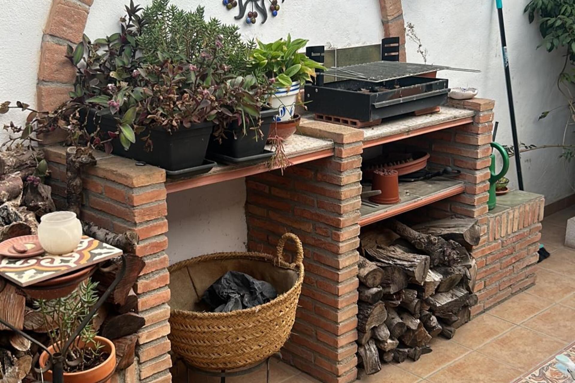 Et udendørs køkken i mursten med grill, blomsterpotter og en flettet kurv.